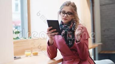 在一家早餐咖啡馆里，一个迷人<strong>的</strong>年轻女孩用她<strong>的</strong>平板电脑触摸她<strong>的</strong>眼镜，微笑着对自己。 时尚<strong>的</strong>服装